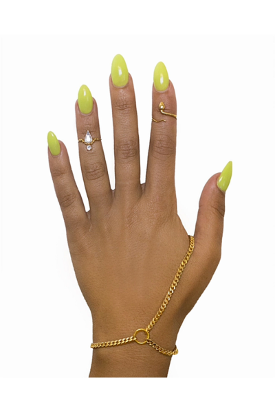 A gold-plated curb link hand chain on a hand with lime green nails, showcasing the adjustable wrist closure and the chain connecting to the middle finger.