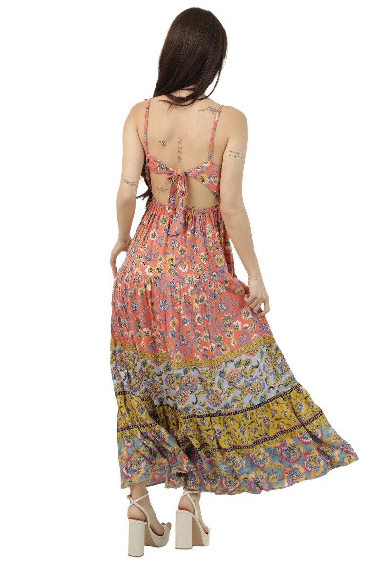 Back view of a coral patchwork‑print maxi dress featuring an open tie‑back, thin straps, and a tiered skirt with blue and gold patterned panels.