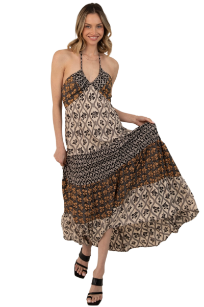 Front view of a mixed‑print halter‑neck maxi dress featuring abstract and geometric patterns in warm earth tones with a flowing tiered skirt.